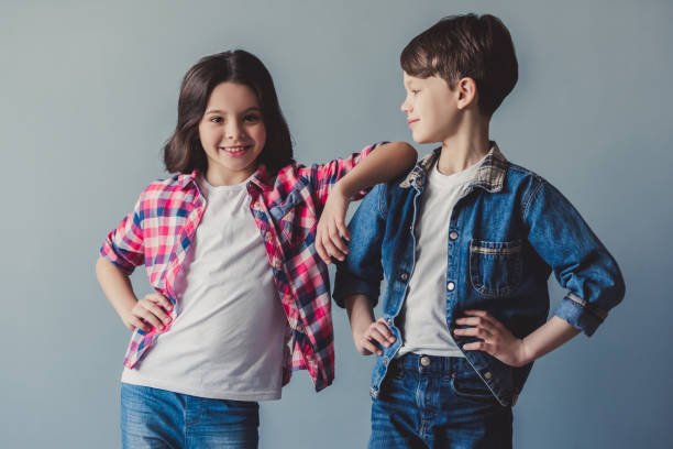 Cute couple of kids in casual clothes are posing and smiling, on gray background